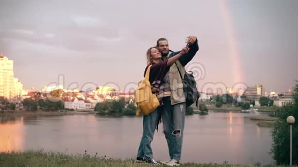 快乐的夫妇在市中心散步并在日落时在智能手机上拍照彩虹和河流的背景视频的预览图