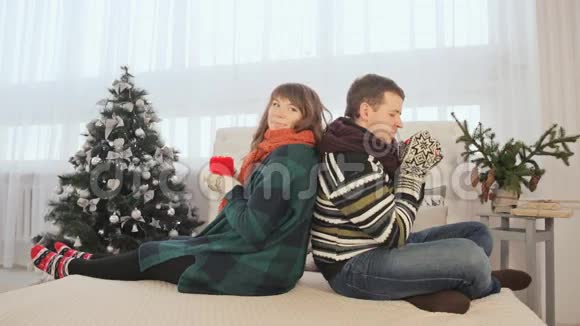 一对相爱的夫妇正背靠背坐在一起喝热咖啡平安夜温暖的新年气氛视频的预览图