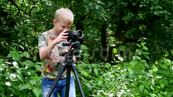 带着摄像机的小男孩拍摄关于绿色公园背景的自然的电影视频的预览图