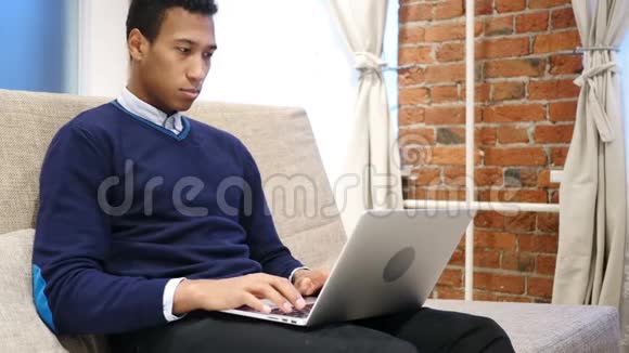 非洲男人思考和工作在笔记本电脑放松沙发视频的预览图