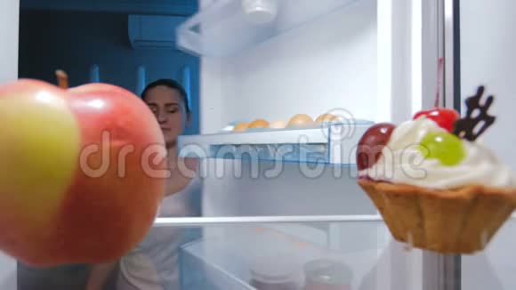 年轻女子晚上从冰箱里拿新鲜苹果的录像适合健康的营养和饮食视频的预览图