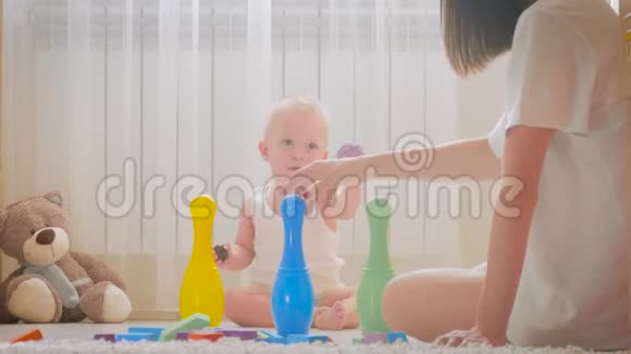 快乐的妈妈和宝宝在家里地毯上玩玩具侧面看一对快乐的母子玩玩具视频的预览图