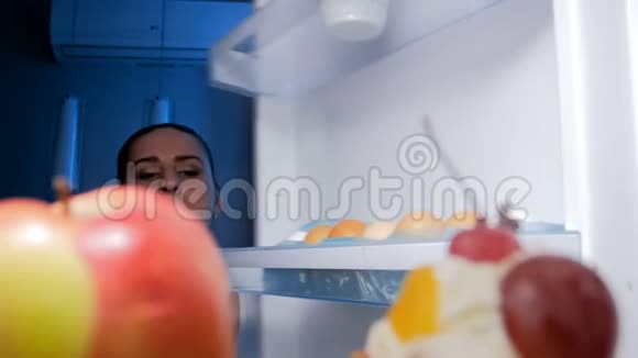 饥饿的微笑女人寻找食物晚上从冰箱里取出甜蛋糕的4K镜头视频的预览图