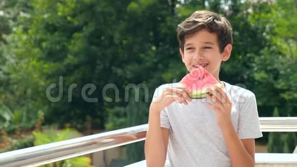 男孩少年在外面吃西瓜背景是绿色和天空4k慢动作视频的预览图