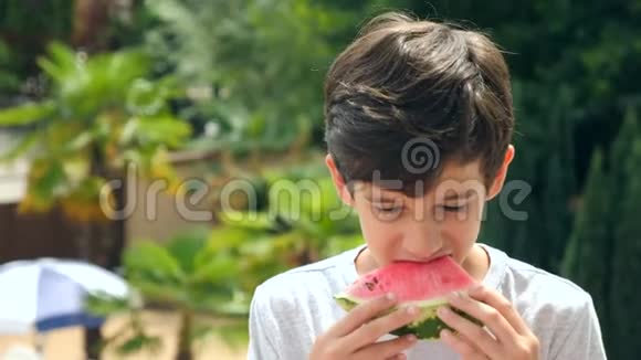 男孩少年在外面吃西瓜背景是绿色和天空4k慢动作视频的预览图