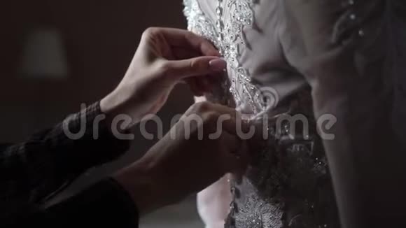 钮扣新娘婚纱特写双手在室内的婚纱上系扣子视频的预览图