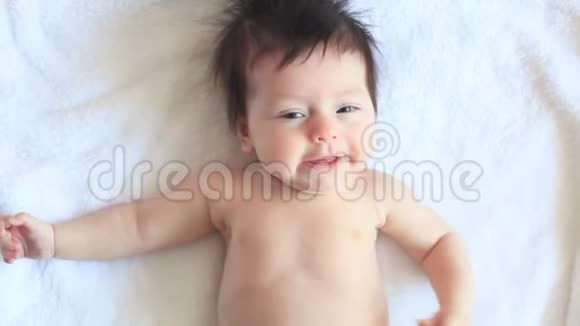 一个可爱的小宝宝正看着相机在一张白色的床单上很开心婴儿环顾四周然后微笑视频的预览图