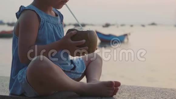 小女孩在日落时慢慢地在海边喝椰子水视频的预览图