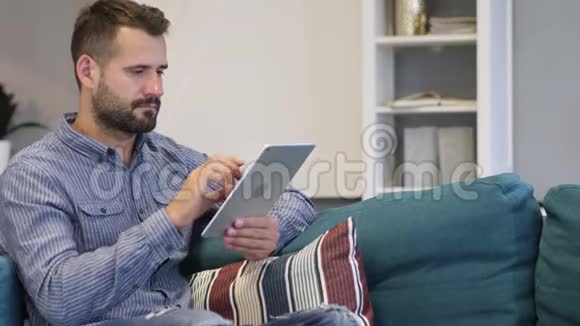 男人在平板电脑上浏览互联网坐在沙发上视频的预览图