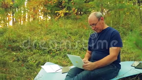一个戴着眼镜的人在林间空地上用笔记本电脑工作视频的预览图