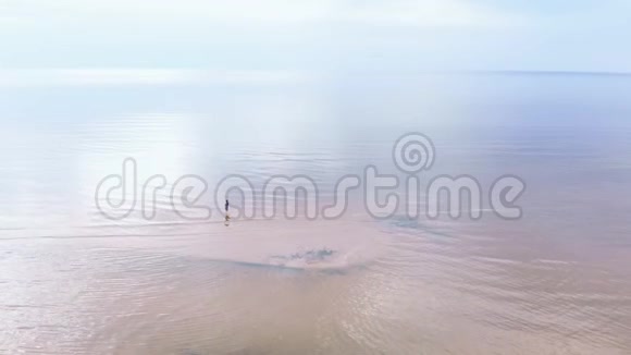 空中穿着蓝色鲜艳连衣裙的年轻女子四处走动浅水景区波罗的海的黄色日落景观视频的预览图
