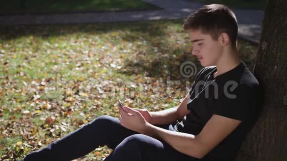 一个男孩坐在树下手里拿着智能手机视频的预览图