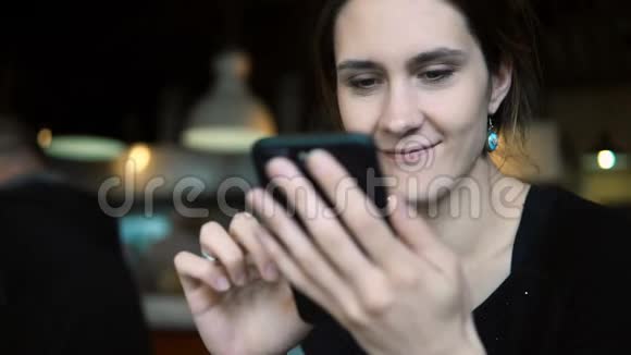 年轻的黑发女人坐在咖啡馆里用智能手机上网视频的预览图
