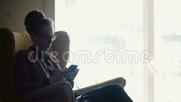 时尚的漂亮女人戴眼镜花时间在互联网上使用智能手机分享空间视频的预览图