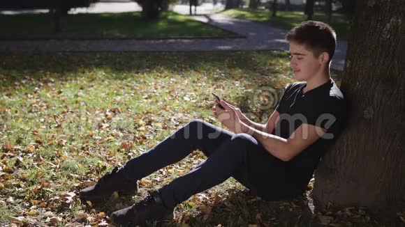一个男孩坐在树下手里拿着智能手机视频的预览图