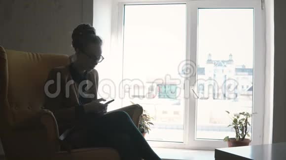 年轻时尚的女人坐在同事的空间里用智能手机上网视频的预览图