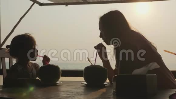 年轻的母亲和女儿坐在海景咖啡馆一起喝椰子视频的预览图