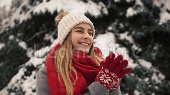 年轻漂亮的女孩穿着温暖的衣服站在圣诞树和温暖的手附近慢动作肖像视频的预览图