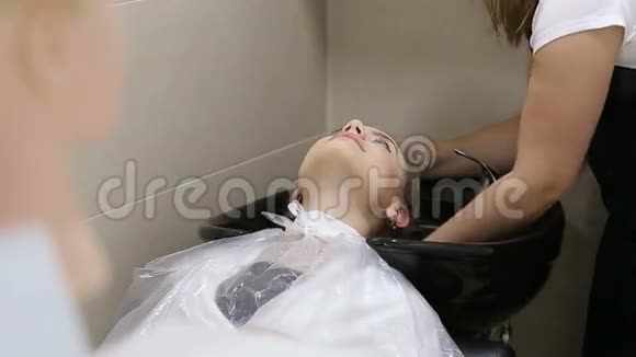 戴手套的理发师给年轻女人洗发廊里的头发视频的预览图