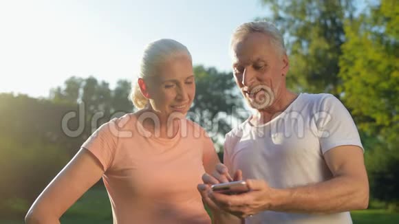 在公园里玩智能手机的快乐运动的老夫妇视频的预览图