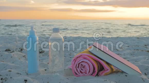 海滩用品一瓶水毛巾太阳镜防晒霜和一本书视频的预览图