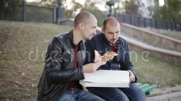 两个人坐在公园长椅上吃着盒子里的外卖披萨视频的预览图