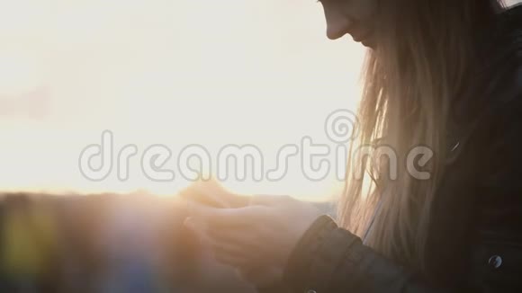 近距离观看日落时站在街道上的年轻女子在等待某人时使用智能手机视频的预览图