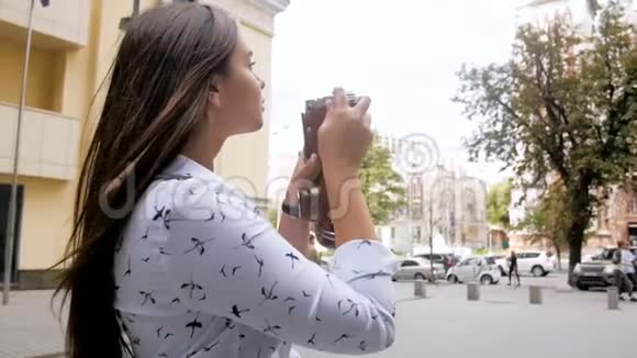 在街上用老式手动摄像机拍摄长头发的美丽黑发女孩的特写慢镜头视频的预览图