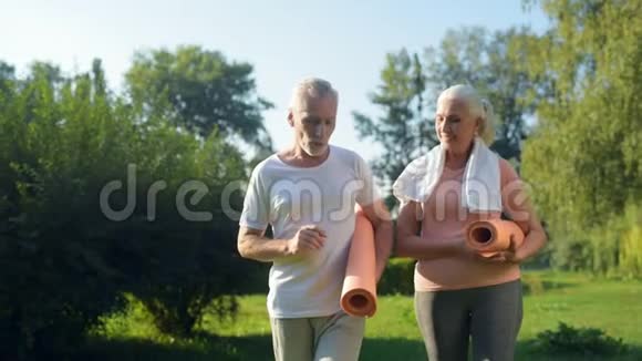 漂亮的老夫妇带着运动垫在公园里散步视频的预览图