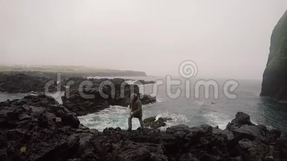 阴天时年轻英俊的男子穿过海边的岩石游客探索新的地方视频的预览图