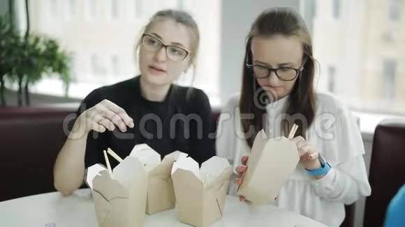 两个戴眼镜的漂亮女人一边吃筷子一边做紧急的生意视频的预览图