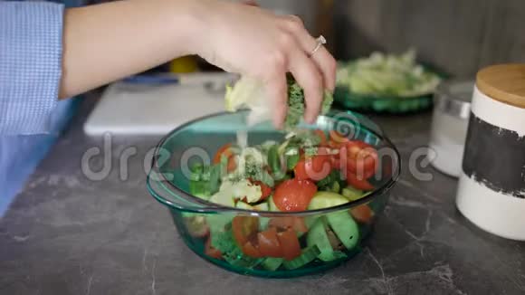 女性手把切好的生菜叶放在沙拉碗里把西红柿和黄瓜放在厨房的桌子上视频的预览图