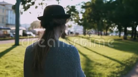 日落时分年轻漂亮的女士戴着帽子在公园里散步使用智能手机在触摸屏上打字视频的预览图