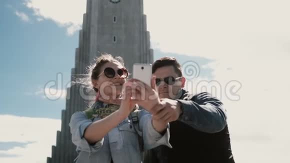 年轻的幸福夫妇在冰岛雷克雅未克的Hallgrimskirkja教堂附近的智能手机上拍摄自拍照片视频的预览图