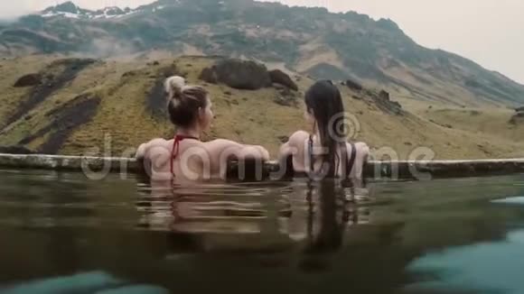 冰岛温泉地热温泉两位旅行妇女在热池中放松山上有美丽的风景视频的预览图