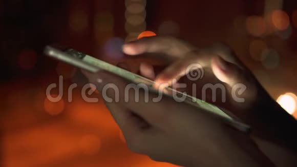 夜间在城市户外使用智能手机触摸屏的女性手部特写浏览信使视频的预览图
