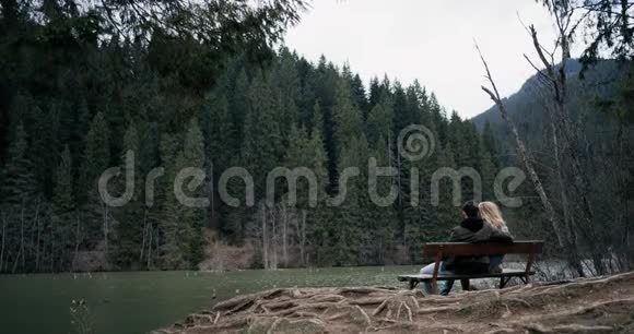 年轻夫妇坐在木凳上看着湖视频的预览图