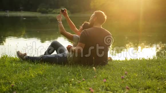 日落时分一对幸福有趣的夫妇在湖边玩智能手机拍照视频的预览图