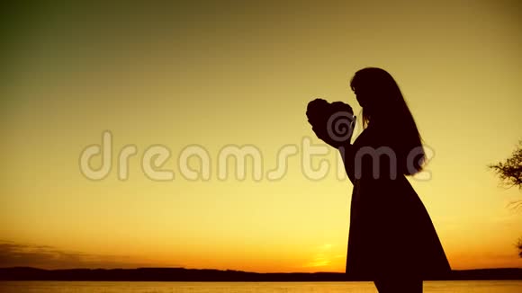 在美丽的夕阳下女孩的剪影紧紧地抓住大海视频的预览图