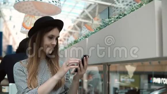 年轻时尚的女人坐在咖啡馆在购物中心和使用智能手机漂亮的女性在触摸屏上打字视频的预览图