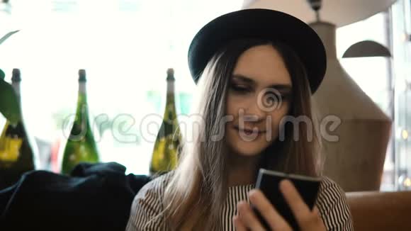 年轻漂亮的女士戴着帽子坐在餐馆里用智能手机上网等待点菜视频的预览图