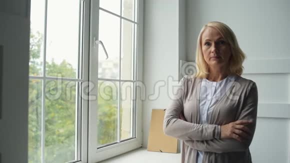 平静的中年妇女站在窗边视频的预览图