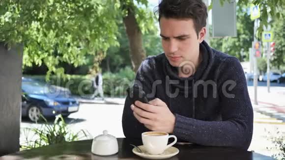 坐在咖啡馆露台上使用智能手机的男人视频的预览图