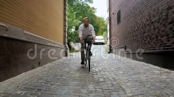 慢动作视频时尚红胡子男子骑自行车沿着老狭窄的街道视频的预览图
