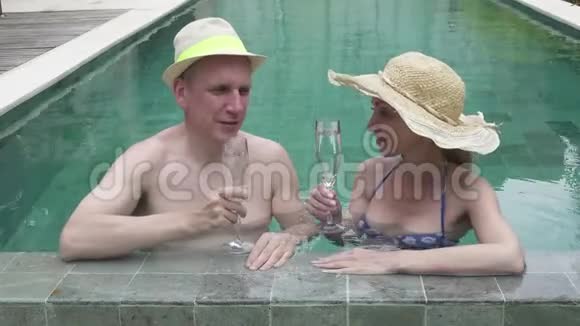 爱的一对夫妇男人和女人在热带度假胜地的游泳池里休息也喝白葡萄酒调色和视频的预览图