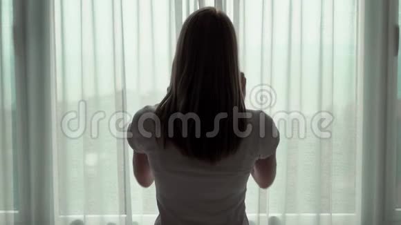 穿白色t恤的女人揭开窗帘看着窗外在外面欣赏海景视频的预览图