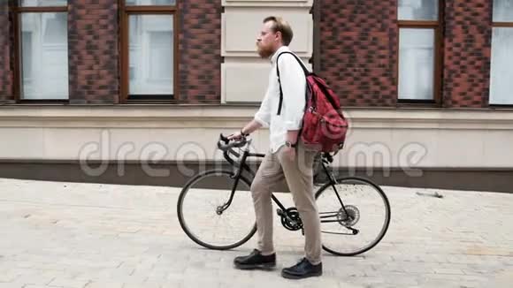 带着红色袋子的小胡子带着自行车在街上行走的慢动作视频视频的预览图