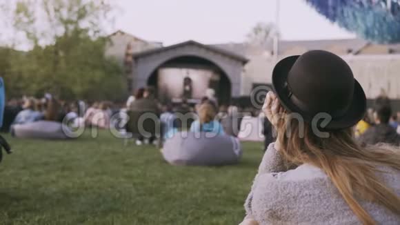 年轻时尚的女士戴着帽子坐在包椅上独自观看露天电影节视频的预览图