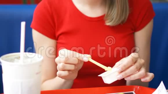 一位饥饿的年轻女士穿着红色T恤坐在咖啡馆里吃着炸薯条蘸着酱汁视频的预览图
