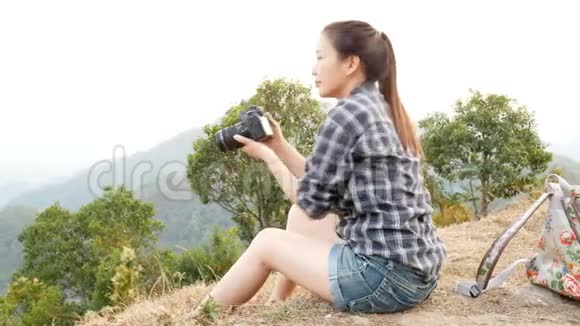 年轻活跃的亚洲旅游女性旅游摄影师带着背包在山上用数码相机拍照视频的预览图